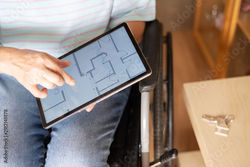 Person in a wheelchair planning their accessible home, viewing a floor plan on a digital tablet, symbolizing independence, mobility, and future living arrangements adapted for disability
