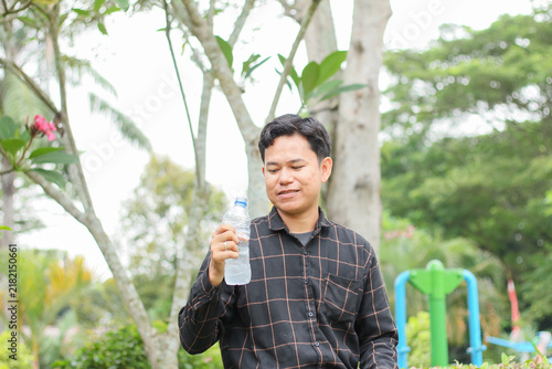 фотографія A young Indonesian man after drinking water; a young Asian man wearing a flannel shirt and staying hydrated with water