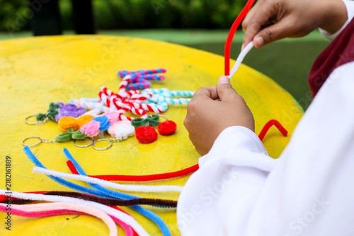 Canvastavla An Indonesian Muslim woman wearing a red hijab making pipe cleaner crafts on a park bench