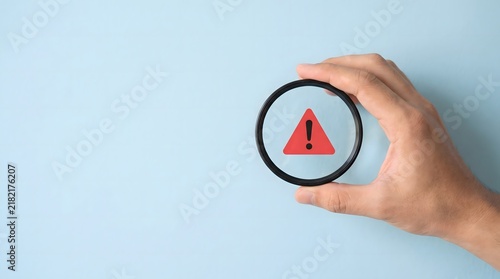 Obraz w ramie Hand Holding Lens Highlighting Red Warning Symbol for Customer Service and Software Bug Detection on Blue Background