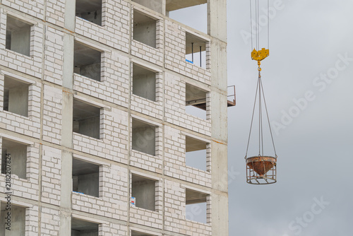 Obraz na płótnie Construction workers elevate a concrete bucket at a building site in the heart of a bustling city under a cloudy sky