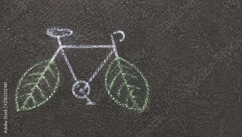Chalk drawing of a bicycle with green leaves as wheels on a dark asphalt surface, emphasizing eco-friendly transportation and artistic expression