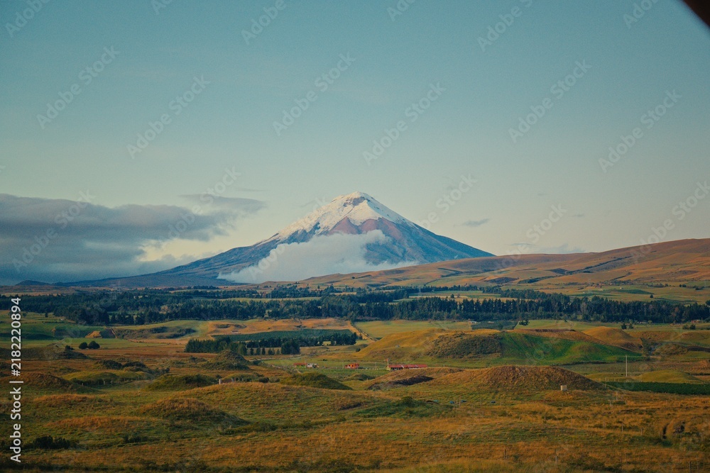 Fototapeta premium Cotopaxi volcano peak with snow and clouds over rolling hills in Ecuador