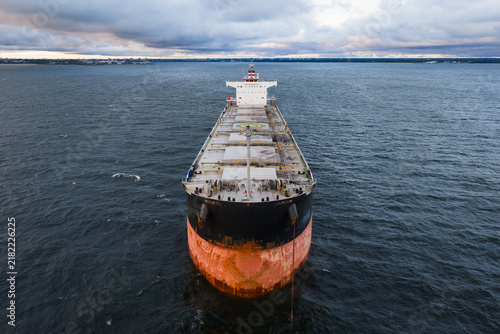 Quadro su tela High angle aerial view of a large commercial bulk carrier cargo ship anchored at sea with its anchor chain lowered into the water