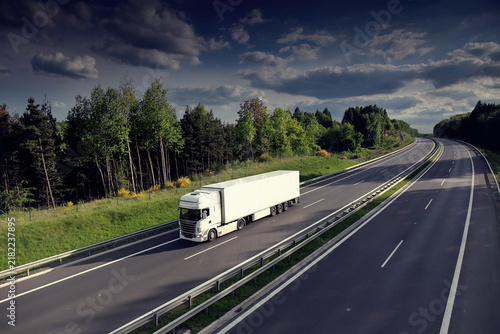 A truck on a highway drives through a wide landscape, transporting goods