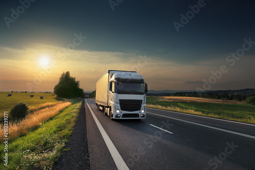 A truck with semi-truck drives through a wide landscape at sunset