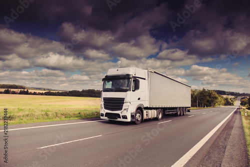 A truck on a highway drives through a wide landscape, transporting goods
