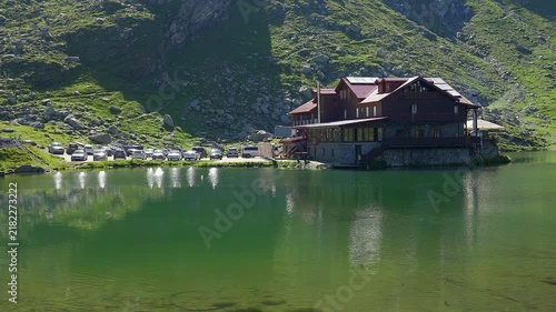 Mountain lodge and parked cars beside the emerald waters of Balea Lake in Romania