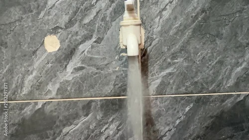 Water Running From Plastic Tap Against Grey Marble Tile Wall