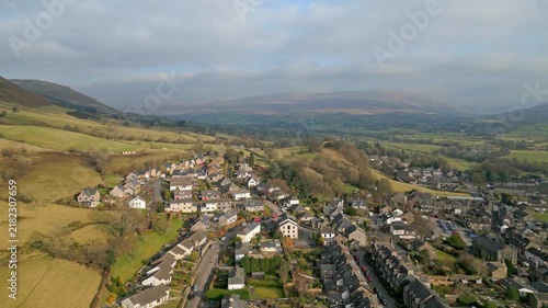 Aerial drone footage of picturesque welsh village nestled within green rolling hills of brecon beacons national park landscape.
