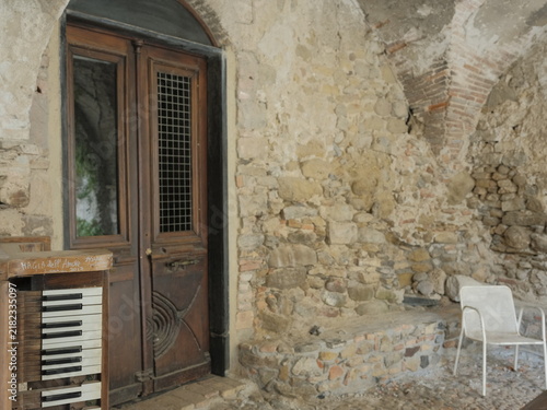 фотографія An abandoned chapel interior featuring a vintage organ, weathered wooden door, exposed stone walls, and deteriorating architectural details