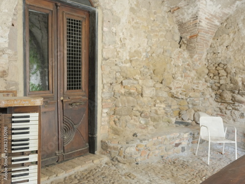 Картината върху платно An abandoned chapel interior featuring a vintage organ, weathered wooden door, exposed stone walls, and deteriorating architectural details