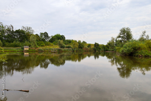 фотографія A calm lake reflects green trees and a cloudy sky in its mirror-like water