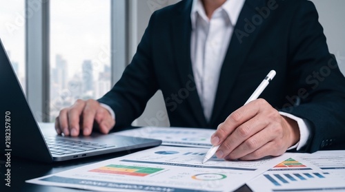 Bild auf Leinwand financial analysis and business reporting concept showing professional reviewing performance charts, revenue metrics, and strategic documents with a laptop and stylus in a corporate environment