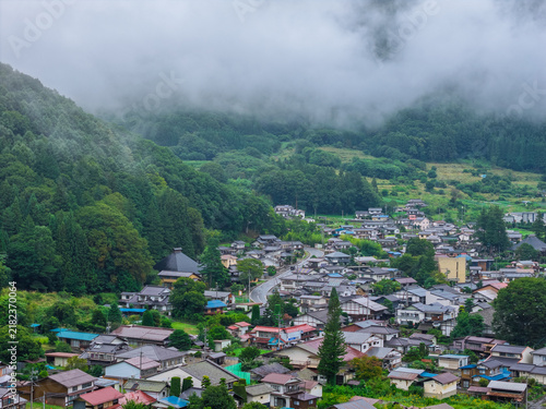 Fog rolls down green forested mountain to traditional Japanese village