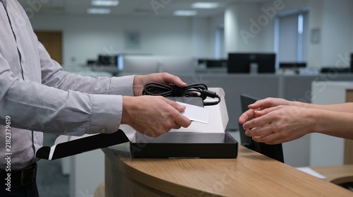 Employee returning company laptop charger cable and access card during IT equipment handover and corporate device offboarding process