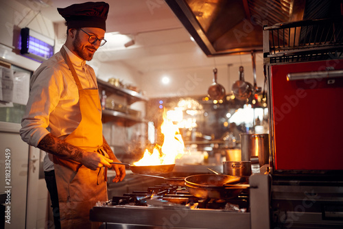 Cook in Professional Modern  kitchen, restaurant concept. Chef and fire in pan.