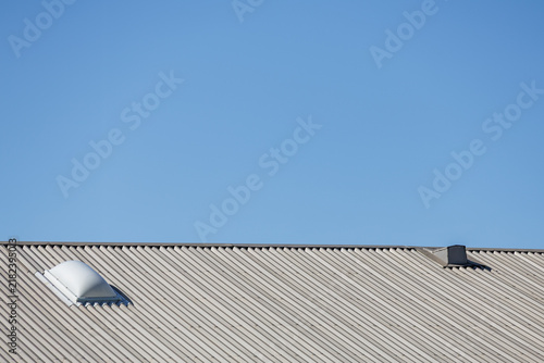 Konstfotografi Low-angle view of an industrial-style corrugated metal roof against a clear blue sky, featuring a domed skylight and the protruding end of a tie rod