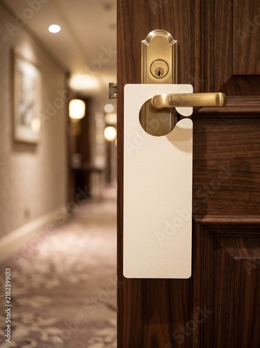 Hotel room door with blank sign hanging on handle in hallway.