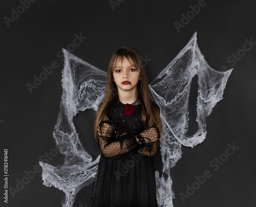 A little girl dressed in a red and black costume as a vampire on Halloween is isolated on a black background with cobwebs. Halloween concept.