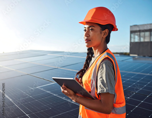 Engineer in protective workwear carrying out service of solar panels with digital tablet on a photovoltaic rooftop plant. Concept of maintenance and setup of solar power station