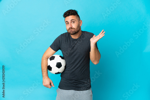 Football player isolated on blue background having doubts while raising hands