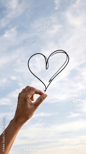 Hand holding a drawn heart against sky