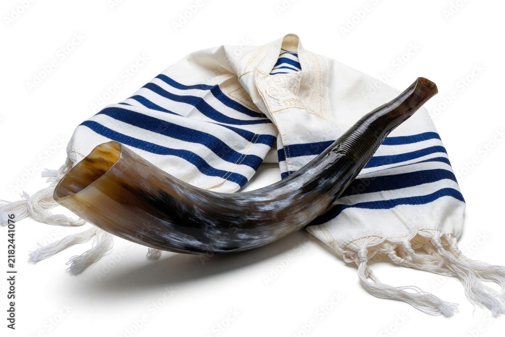 Obraz premium Jewish shofar horn rests on white tallit prayer shawl. Traditional ritual objects for Rosh Hashanah, Yom Kippur holidays. Religious items isolated on white background for Jewish New Year celebration.