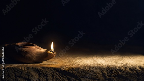 Ancient clay oil lamp burning with flame on old stone table in darkness. Biblical times light in dark night. Faith and hope concept. Miracle of Jesus at wedding in Cana of Galilee. Copy space