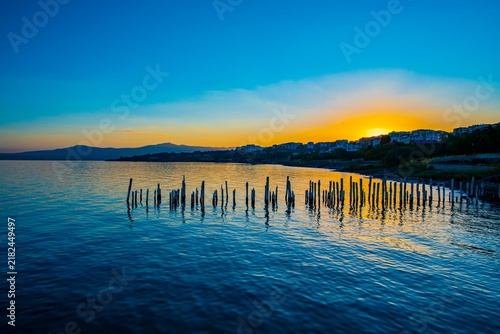 Scenic long exposure view of the weathered wooden poles from a ruined old pier on the peaceful coast of Lake Van during golden sunset. Beautiful natural landscape of Eastern Anatolia with calm water s