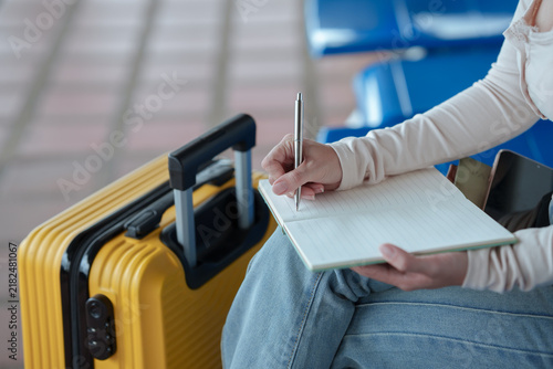 Фотография Traveler writing notes in a notebook beside a suitcase at an airport, representing travel planning, itinerary preparation, vacation organization, and journey preparation