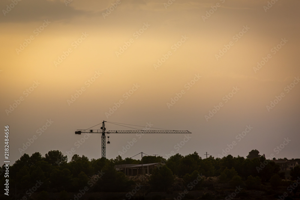 Fototapeta premium Construction Crane Silhouetted Against a Golden Sunset Sky in Moraira, Costa Blanca, Spain