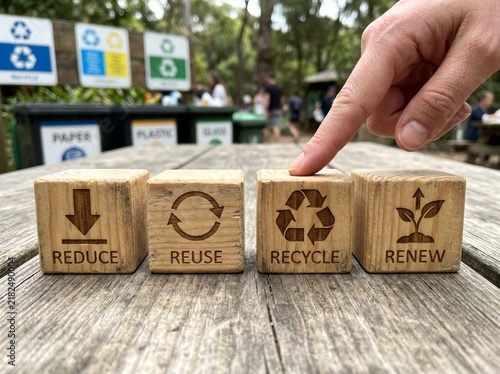 Human hand points toward wooden blocks featuring engraved symbols for reduce reuse recycle and renew concepts on a rustic table
