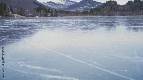 Aerial drone view moving forward over smooth frozen lake ice during winter season.