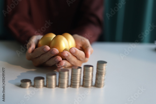 Quadro su tela Rising stack of coins on the table and golden eggs on businessman's hand
