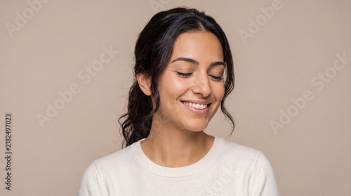 Young woman smiling with eyes closed in a moment of peace and meditation on neutral beige background
