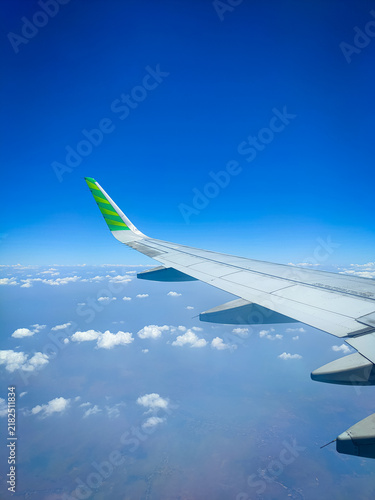 Airplane wing view from window seat, bright blue sky with fluffy white clouds below, green-yellow winglet, flying high above the horizon. Perfect travel and aviation scene, portrait view. 