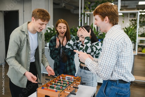 Obraz na plátně Excited young colleagues playing table football in the office during break time