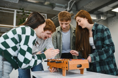 Fotografie Excited young adults playing table football together in modern office