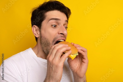 Фотография Excited Expression Young Caucasian Man Eagerly Preparing To Take Big Bite Of Burger Surrounded By Bright Kitchen