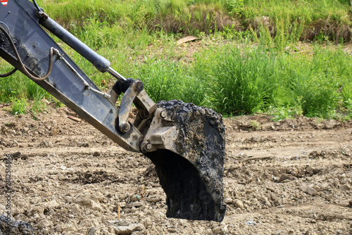 Heavy excavator bucket lifts clumps of dark soil at active construction site