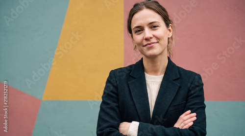 Confident businesswoman standing with crossed arms against a colorful geometric wall for leadership concept