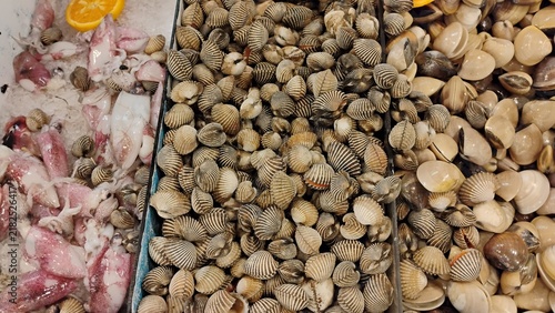Bild auf Leinwand Top-down of fresh seafood displayed on crushed ice in a market, featuring raw squid, blood cockles, and various clams in separate metal bins