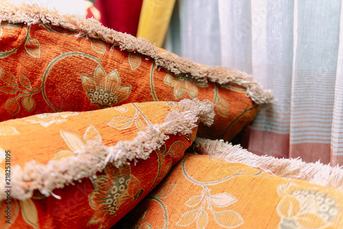 Foto Close-up of orange patterned fabric cushions with fringe details stacked on a sofa indoors