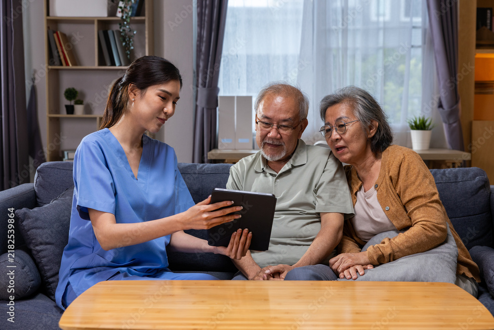Obraz premium Asian nurse elderly couple tablet living room healthcare conversation Asian nurse helps elderly couple use tablet comfortable living room, creating supportive home care moment filled with trust
