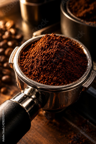 Freshly Ground Coffee Powder in Espresso Portafilter with Roasted Beans Background