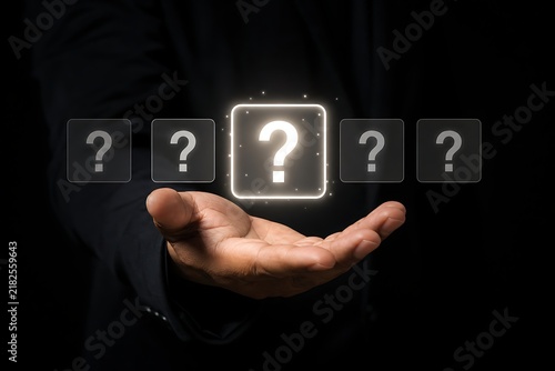 Business person holding a glowing question mark icon in their hand against a dark background