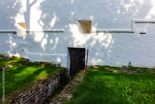 Fotografie Massive white monastery fortress wall with a rustic dark metal door and narrow d