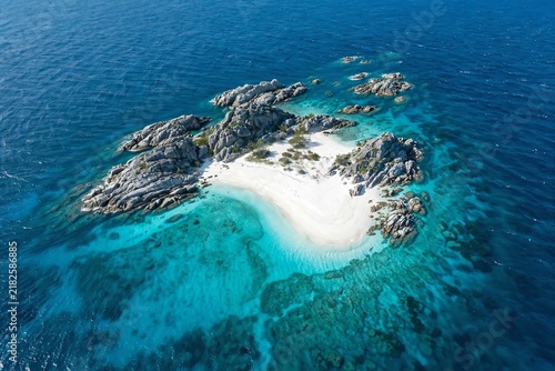 A spectacular aerial perspective of a tiny isolated island featuring white sandy shores, rugged granite rock formations, and clear turquoise lagoon waters surrounded by deep blue ocean.