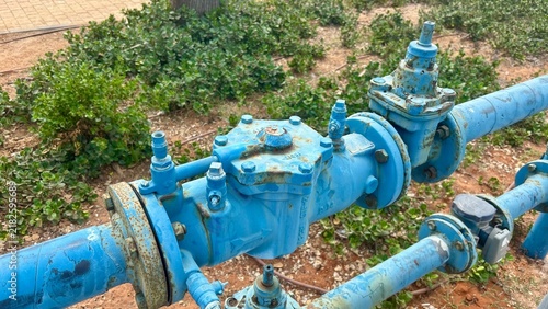 Foto Blue water pipe and industrial valve installed beside a sandy landscaped area in